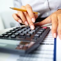 Photo of hands holding pencil and pressing calculator buttons over documents