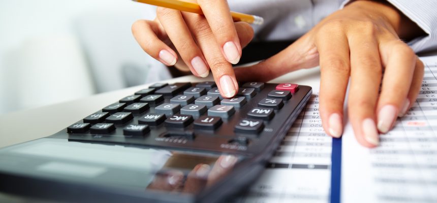 Photo of hands holding pencil and pressing calculator buttons over documents