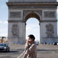 Uma mulher usando uma máscara protetora caminha perto do Arco do Triunfo enquanto a França enfrenta um surto de doença por coronavírus (COVID-19), em Paris