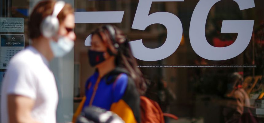 People, wearing protective face masks, walk past a 5G data network sign at a mobile phone store in Paris, France, April 22, 2021. REUTERS/Gonzalo Fuentes